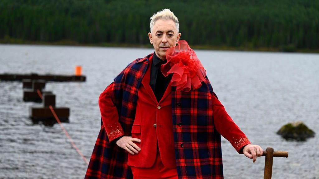 Alan Cumming facing camera in a vibrant red suit