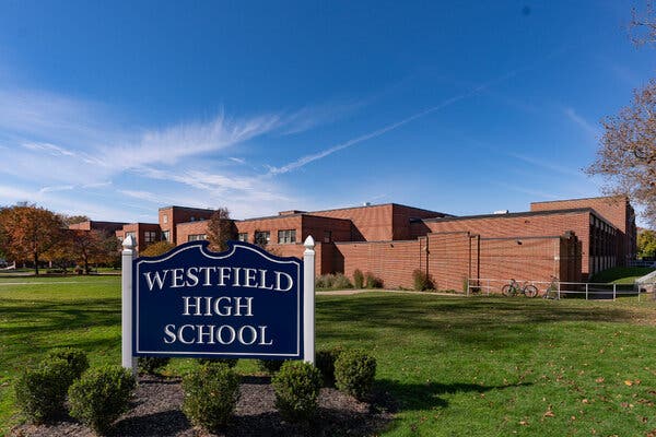 A blue sign on manicured grounds says, “Westfield High School.” In the background, a large, low brick building sits under a blue sky. 